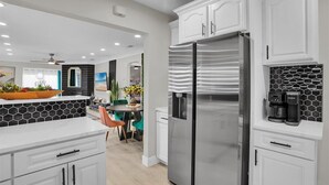 Una cocina moderna con armarios blancos, un refrigerador de acero inoxidable y una cafetera sobre la encimera.