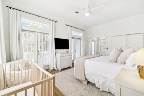 A bright, white-themed bedroom with a crib, a bed, a dresser, and a television. - 🏖️ Coastal Decor | Pool | Bikes | Ping-Pong Table 🏓 (Seagrove)
