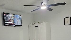 A hotel room with a bed, a wardrobe, a ceiling fan, and a TV displaying a program. - Private Suite Independent Entrance, All Amenities (Kissimmee)