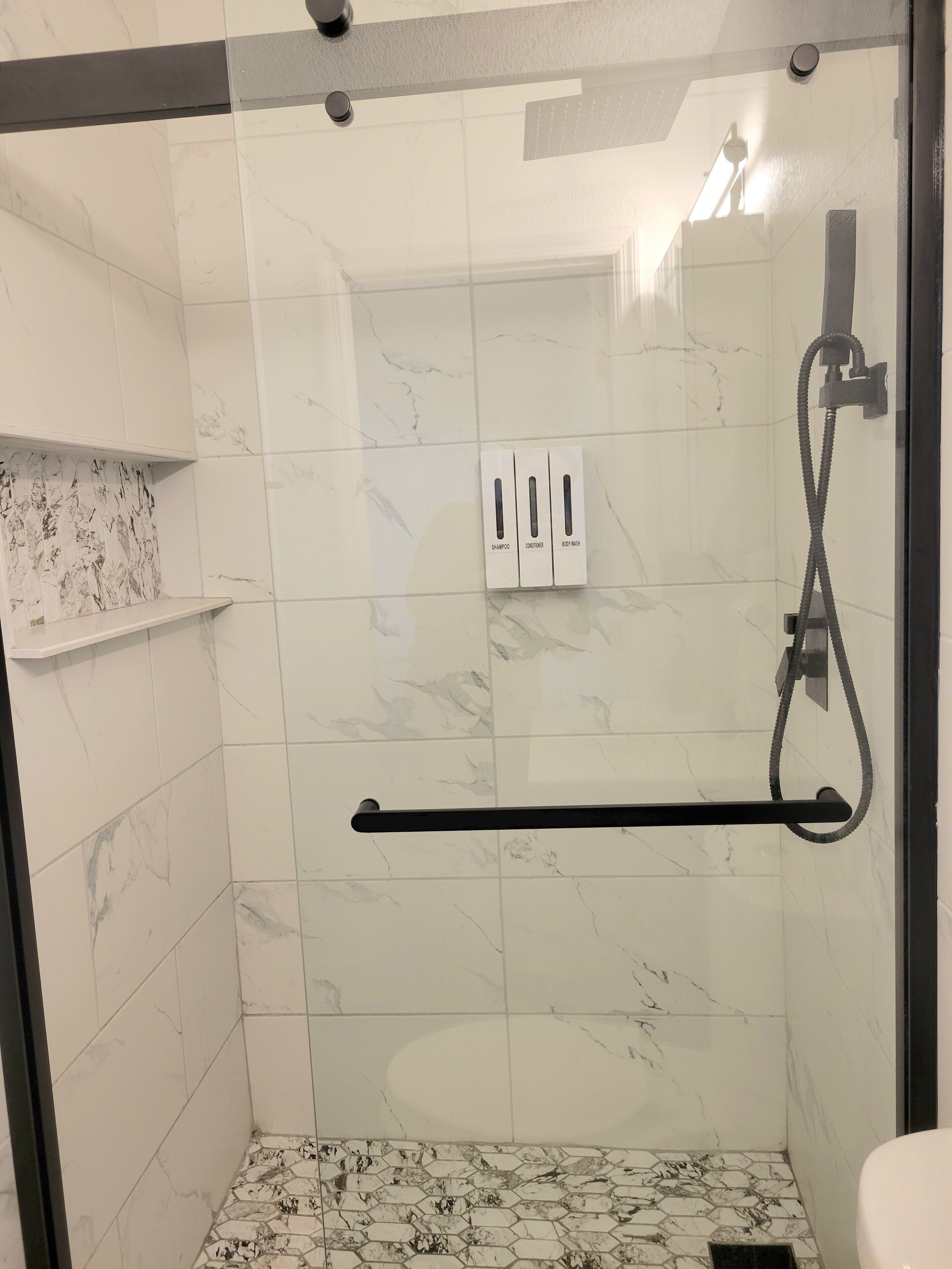 A modern bathroom with a glass shower enclosure, white marble tiles, and a black towel rack.