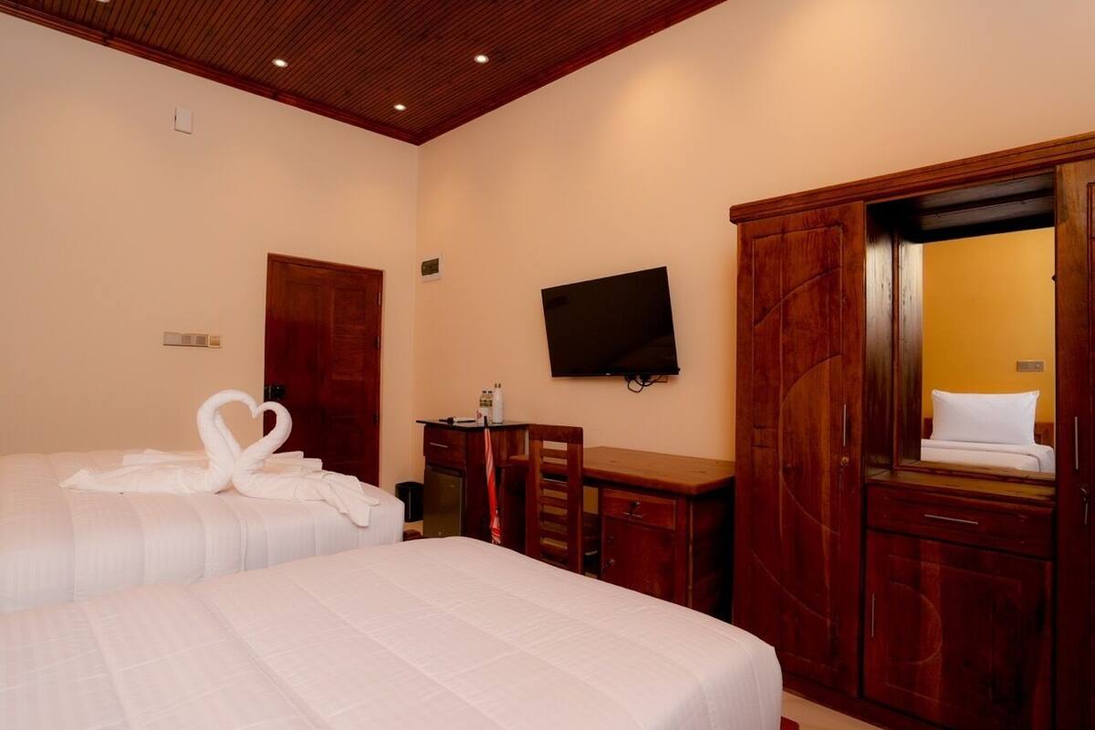 A hotel room with two beds, a TV, wooden furniture, and a mirror.