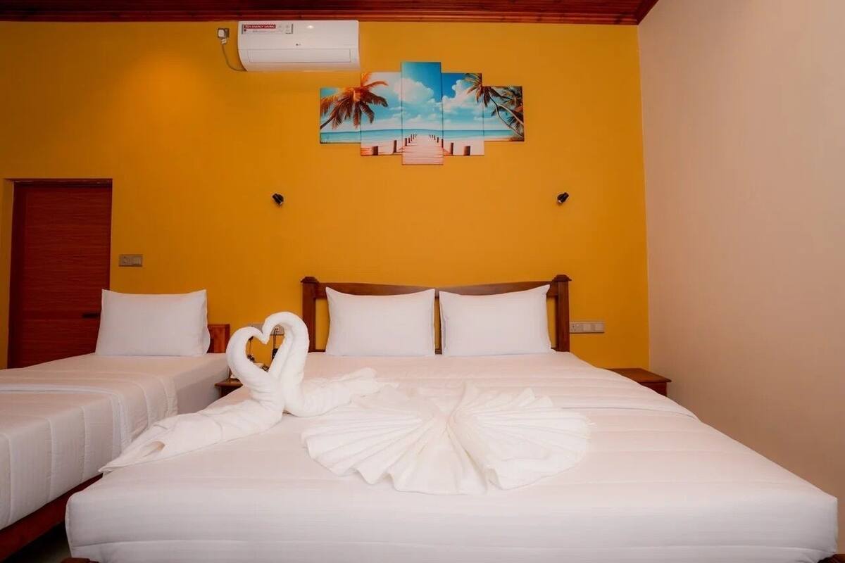 A hotel room with two beds, a wooden ceiling, and a tropical-themed painting on the wall.