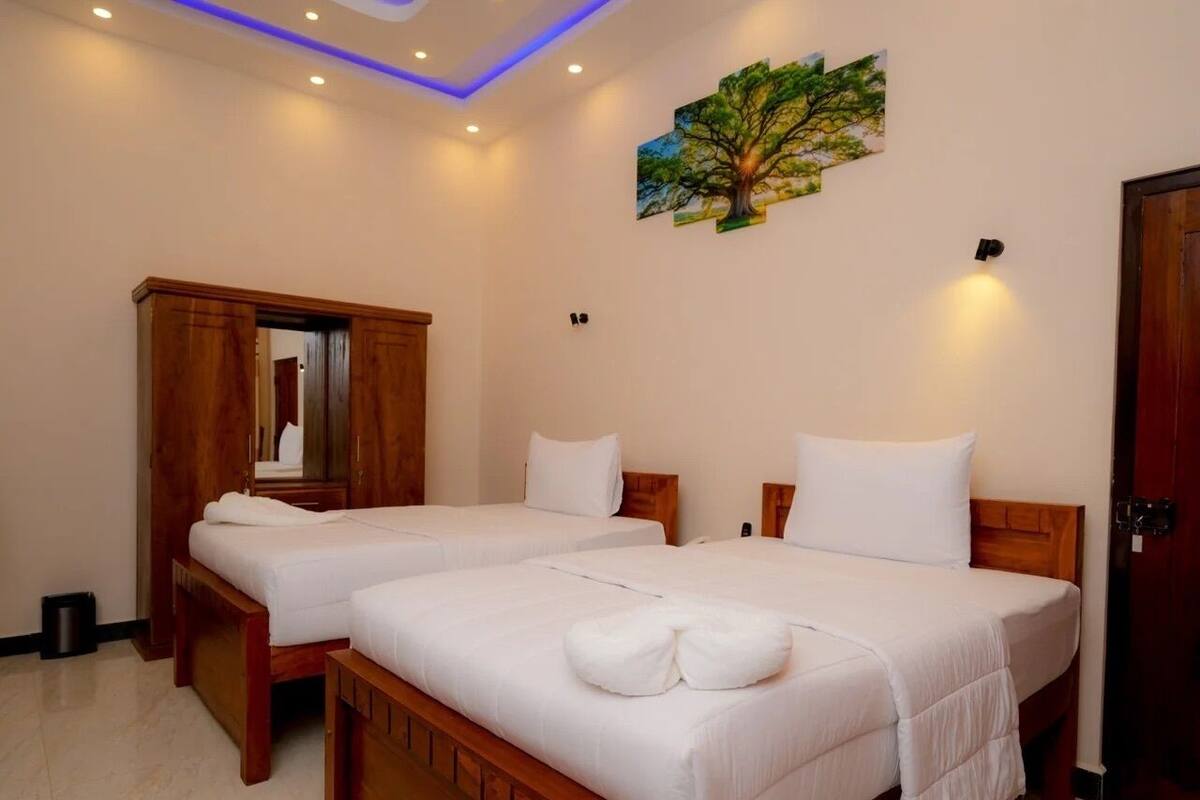 A hotel room with two wooden beds, white bedding, a wooden wardrobe, a mirror, and a wall-mounted artwork of a tree.