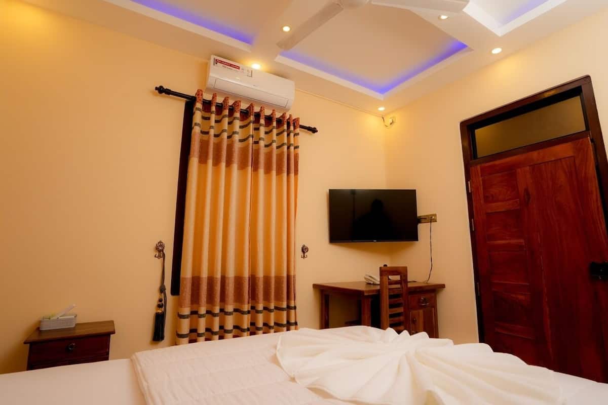 A hotel room with a bed, a desk, a television, and a wooden door.