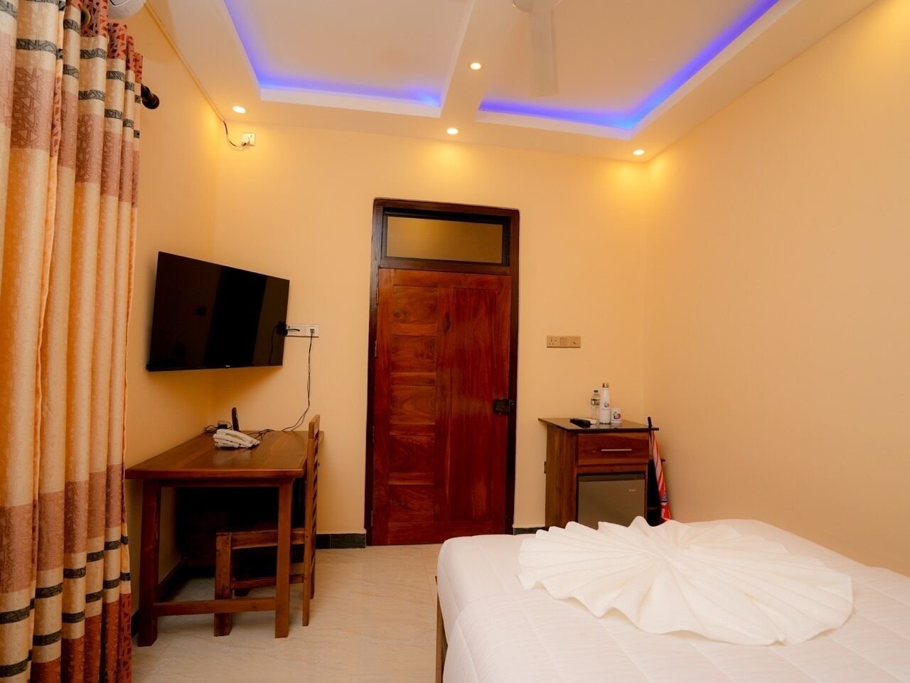 Habitación de hotel con cama, escritorio con silla, televisor montado en la pared y puerta con espejo.