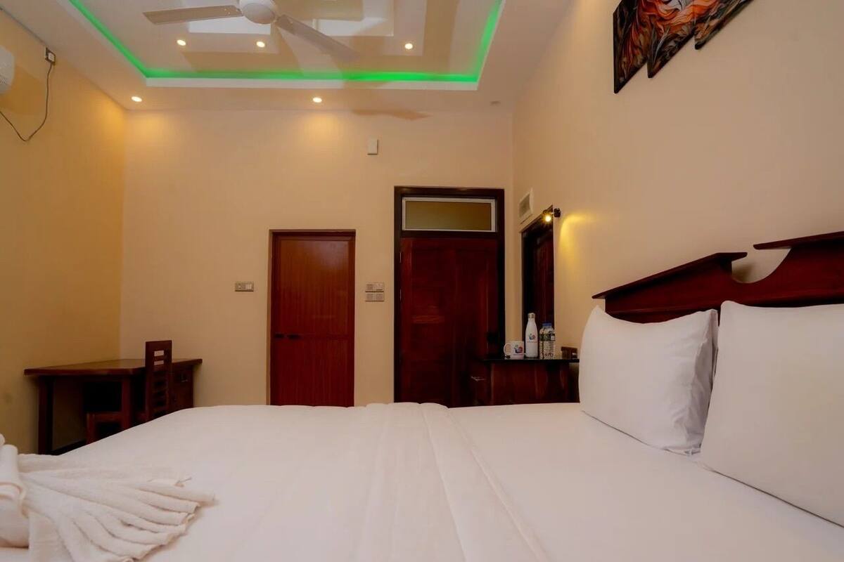 A hotel room with a bed, a desk, a chair, a wardrobe, and a ceiling fan.