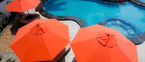 Une piscine entourée de plusieurs bains à remous, de parasols orange et de chaises longues.