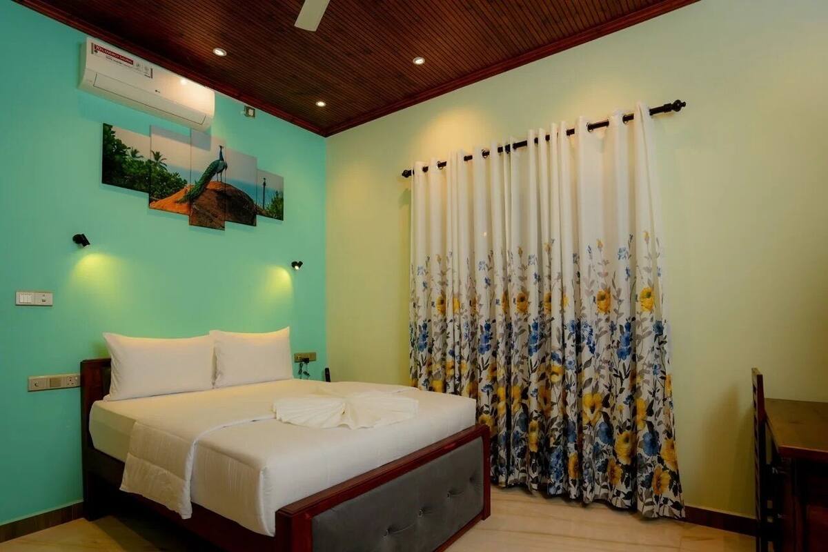A bedroom with a bed, a floral curtain, a wall-mounted air conditioner, and a painting.