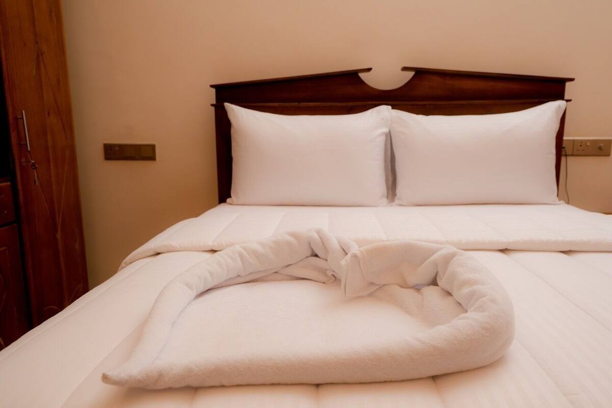 A neatly made bed with a white blanket and pillows, a wooden headboard, and a wooden door to the left.