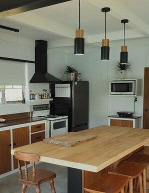 Eine moderne Küche mit einer zentralen Kochinsel, Holzschränken, einem Herd, einem Kühlschrank und Pendelleuchten.