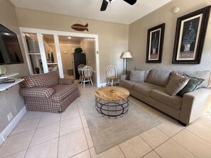 A living room with a sofa, a round coffee table, and a TV. There is a door leading to another room. - Lakefront 1920s 1-bedroom / 1-bath apartment at Villa Lotela - Apt. # 4 (Avon Park)