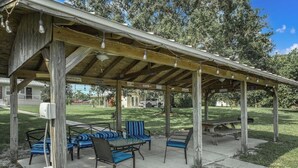 Une terrasse extérieure dotée d’une pergola en bois, d’un espace salon avec des chaises et des tables, et d’une table de pique-nique.