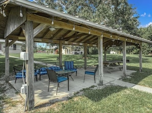 An outdoor patio with a wooden pergola, seating area with chairs and tables, and a picnic table.