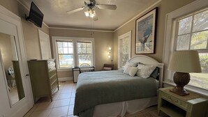Une chambre à coucher comprenant un lit, une commode, une table de chevet, un ventilateur de plafond et une fenêtre avec des stores.