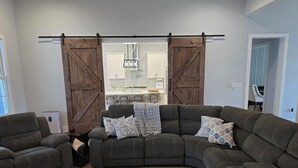 Een moderne woonkamer met een hoekbank, een bijzettafeltje en een schuifdeur van hout die leidt naar een keuken.