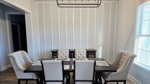 Een eetkamer met een rechthoekige tafel, zes gestoffeerde stoelen en een moderne kroonluchter.