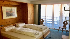 A hotel room with two beds, a wooden headboard, a framed picture on the wall, and a balcony with a view. - Derby 31 by Interhome (St. Moritz)