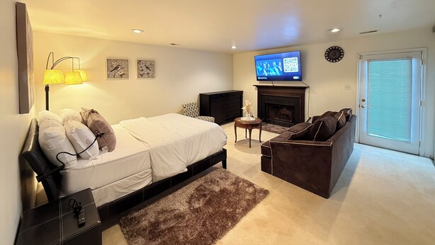 A hotel room with a bed, a sofa, a TV, a fireplace, and a door with blinds. - Cozy 1-bedroom studio in tranquil Laurel with AC (Laurel)