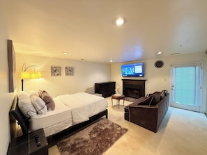 A hotel room with a bed, a sofa, a TV, a fireplace, and a door with blinds.