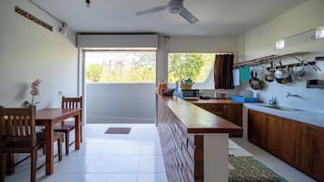 A modern kitchen with a dining area, a ceiling fan, and a view of greenery outside.