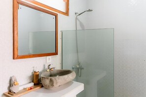 Une salle de bain avec un lavabo en pierre, un miroir et une cabine de douche en verre.