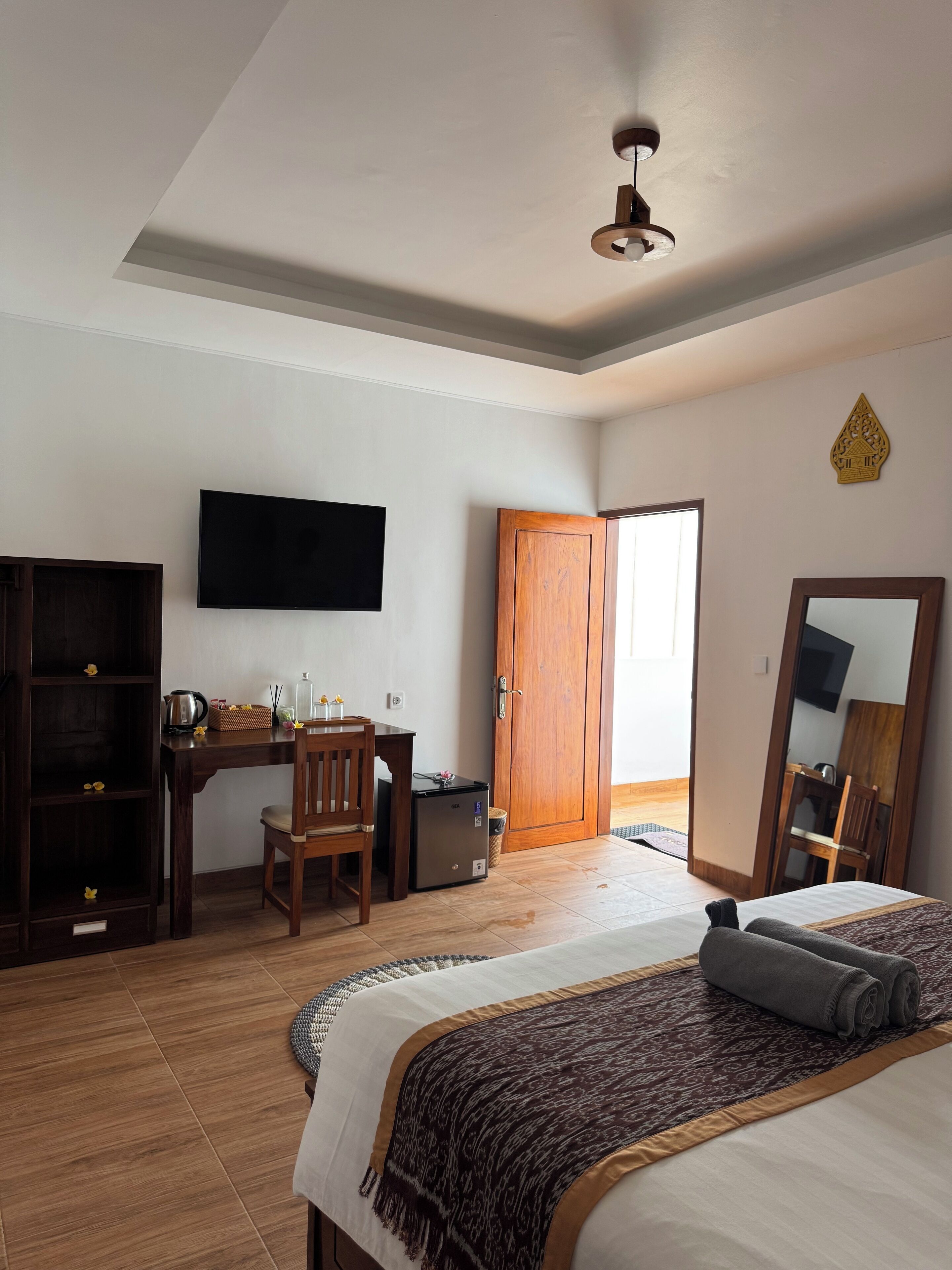 A bedroom with a bed, a desk, a chair, a television, a wardrobe, and a door leading to another room.