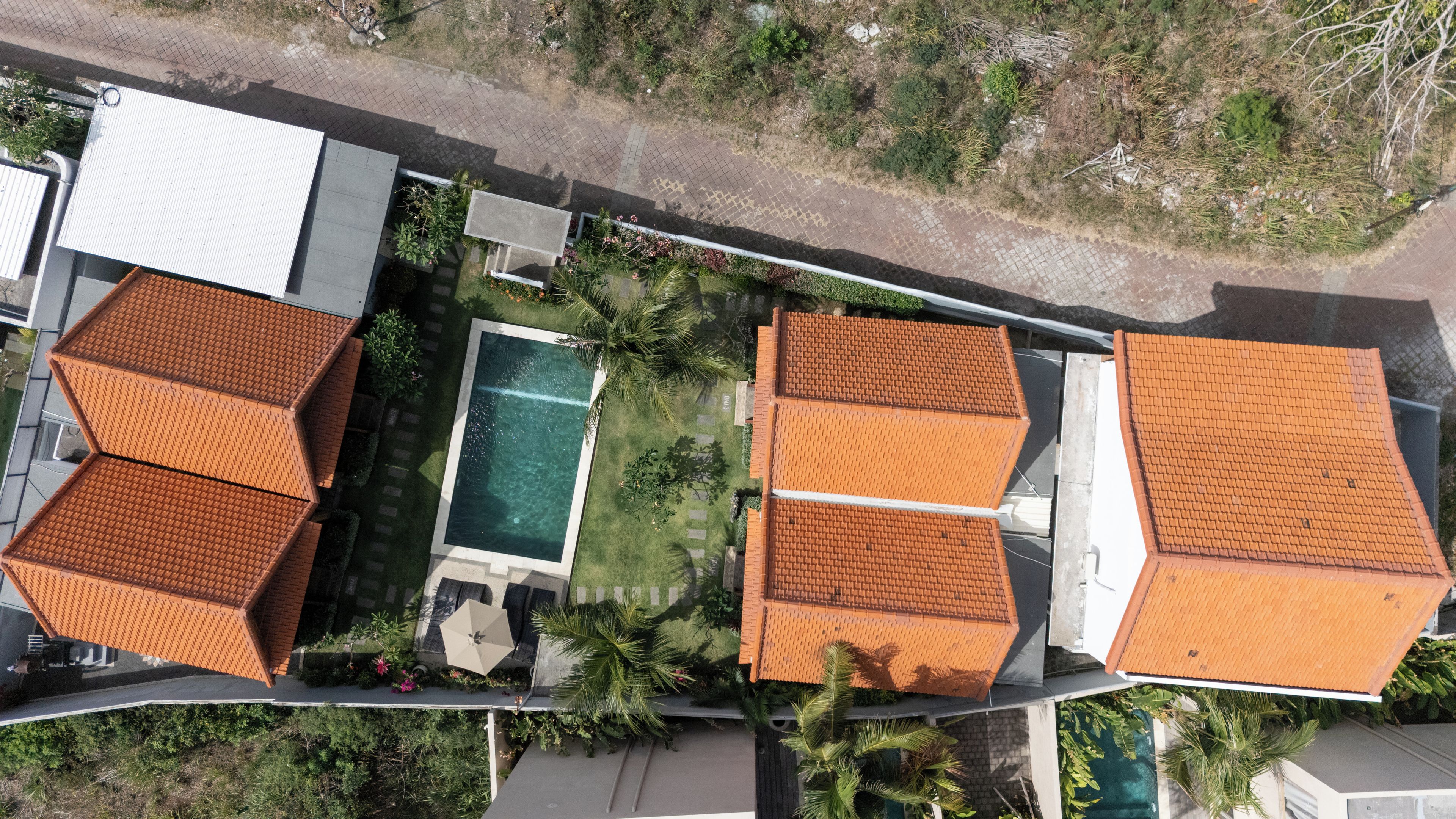 An aerial view of a residential area with multiple houses, a swimming pool, and a paved walkway.