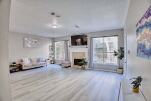 A spacious living room with a fireplace, large windows, and a flat-screen TV.