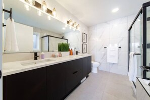 A modern bathroom with a large mirror, a black vanity, a toilet, and a glass shower enclosure. - Skyline Serenity | HotTub | Rooftop Patio |Central (Edmonton)