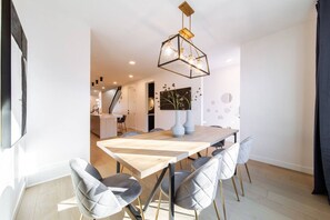 A modern dining area with a wooden table, grey upholstered chairs, and a geometric pendant light. - Skyline Serenity | HotTub | Rooftop Patio |Central (Edmonton)