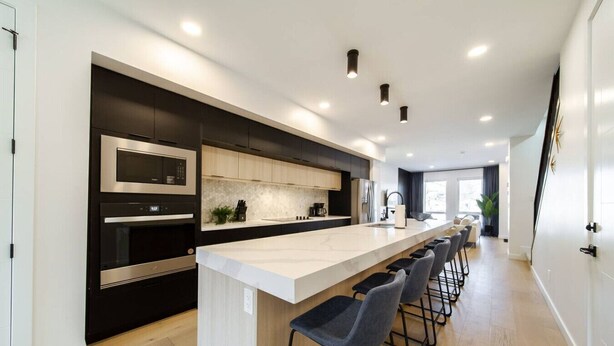 Una cocina moderna con una isla central, taburetes de bar y electrodomésticos integrados.