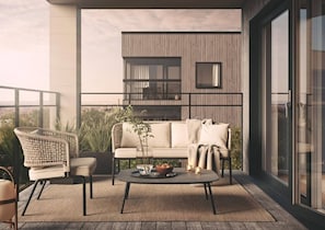 Un espacio al aire libre moderno con un sofá, un sillón y una mesa de centro, con vistas a un edificio con amplios ventanales y un balcón.