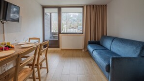 Habitación con una mesa de comedor, sillas, un sofá azul, un televisor en la pared y una ventana con cortinas.