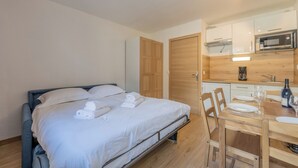 Un dormitorio con cama, piso de madera, una kitchenette pequeña y un comedor con mesa y sillas.
