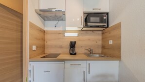 Una cocina compacta con armarios blancos, microondas integrado, cafetera y lavavajillas.
