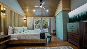 A bedroom with a wooden ceiling, a bed with a bench, a dresser, and a painting on the wall. - Modern 2BR Creekside Cottage, Minutes to Pigeon Forge, No steep roads (Sevierville)