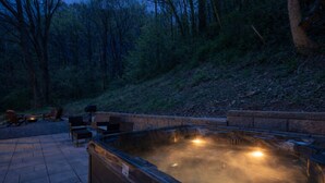 A hot tub surrounded by stone seating and a fire pit, set in a forested area. - Modern 2BR Creekside Cottage, Minutes to Pigeon Forge, No steep roads (Sevierville)