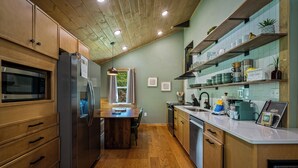 A kitchen with wooden cabinets, a stainless steel refrigerator, a wooden dining table, and a window with curtains. - Modern 2BR Creekside Cottage, Minutes to Pigeon Forge, No steep roads (Sevierville)