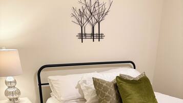 A neatly made bed with a white quilt, a bedside table with a lamp, and a wall decoration.
