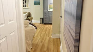 Een gang met houten vloer die uitkomt in een slaapkamer met een bed en een dressing.