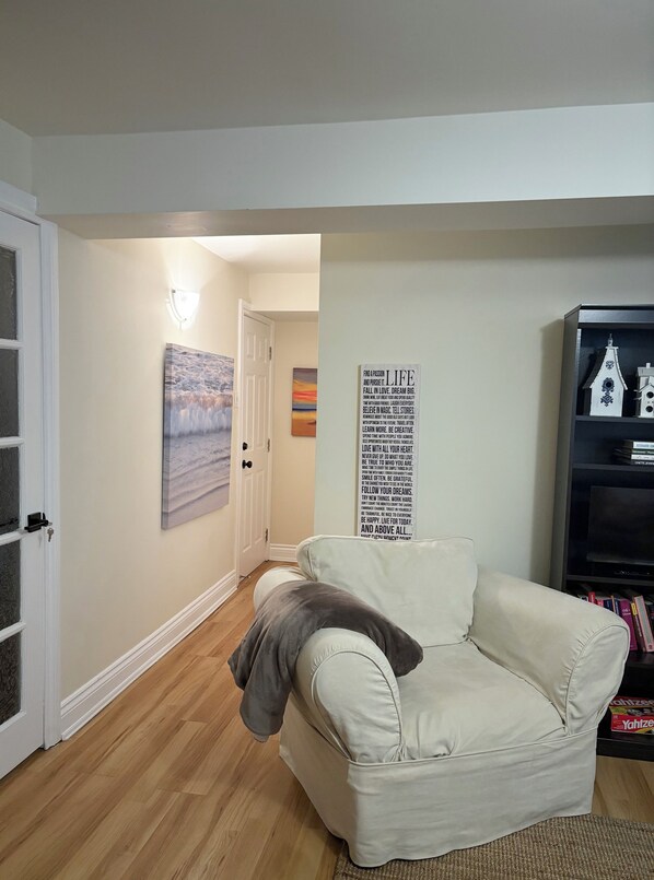 A living room with a beige couch, a wall with a motivational quote, and a bookshelf with books and a model house.