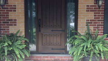 A brick building with a wooden door, two potted ferns, and a brick-paved entrance.