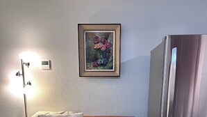 A living room with a leather sofa, a glass coffee table, a framed painting, a modern stainless steel refrigerator, and a floor lamp.