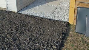A white house with a gravel driveway and a wooden fence.