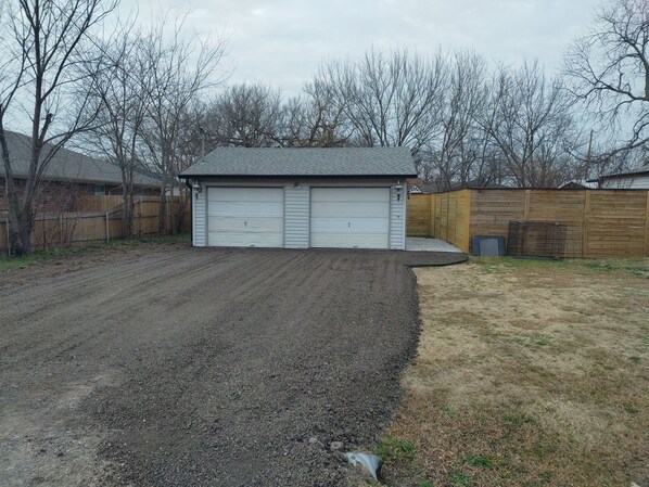 Eine Garage mit zwei weißen Türen, einer Schotterauffahrt und einem Holzzaun.
