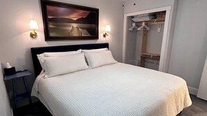 A bedroom with a bed, a ceiling fan, a painting, and a nightstand.