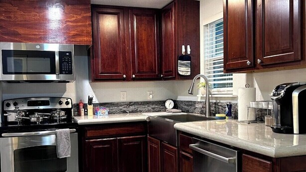 A kitchen with dark wooden cabinets, stainless steel appliances, a marble countertop, and a built-in dishwasher.