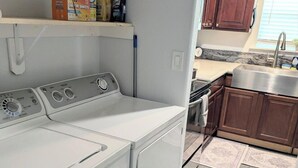 A compact laundry area with a front-loading washer and dryer, a countertop with cleaning supplies, and a small sink.