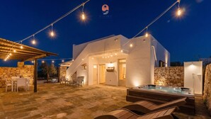Et moderne hus med stenvæg, jacuzzi, udendørs møbler og lyskæder.