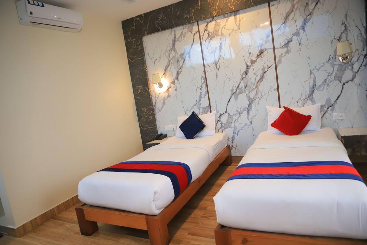 Dos camas individuales con ropa de cama blanca, corredores de cama a rayas azules y rojos, y una pared con estampado de mármol.